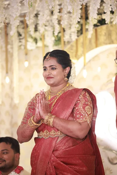 Bride in red silk with an embroidered blouse, hands joined in greeting