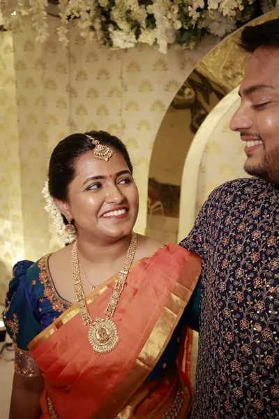 Bride in orange silk with a blue blouse, laughing with the groom