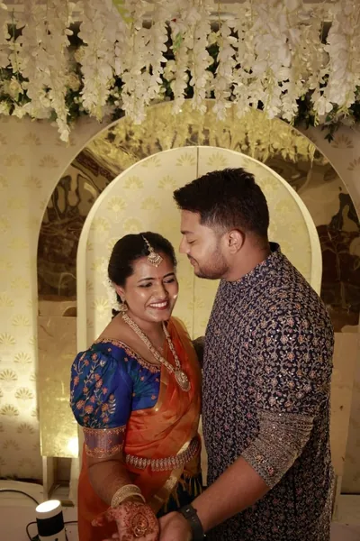 Bride in orange silk with a blue blouse beside the groom